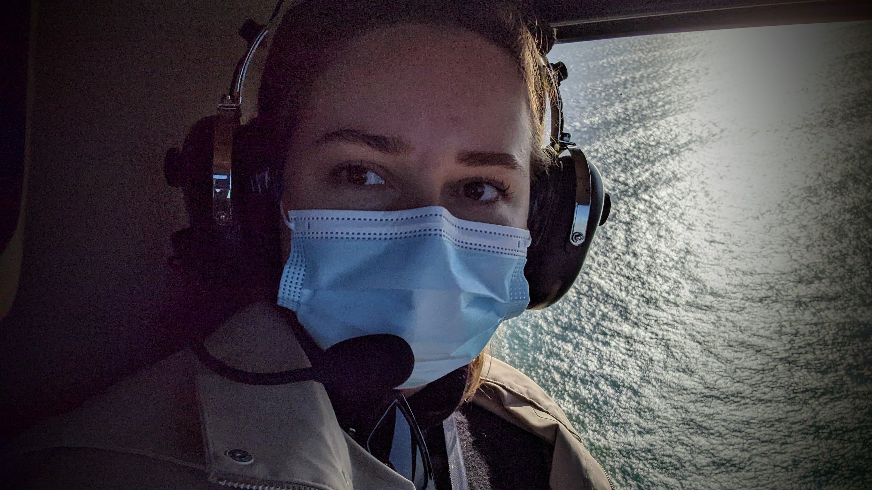 Person wearing headphones and a face mask inside an aircraft, looking out the window. Anna Muratova, pen plotter artist.